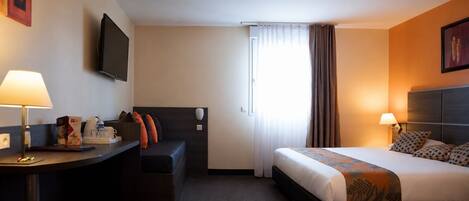 A hotel room with a bed, a desk, a chair, a television, and a window with curtains.
