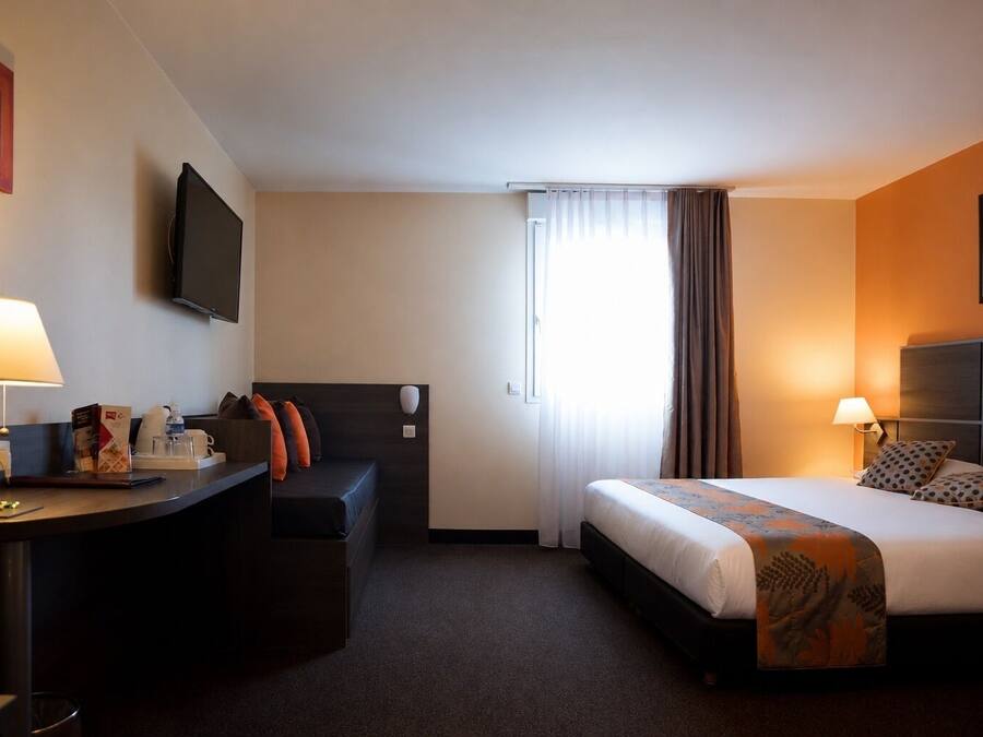 Habitación de hotel con cama, escritorio, silla, televisión y ventana con cortinas.