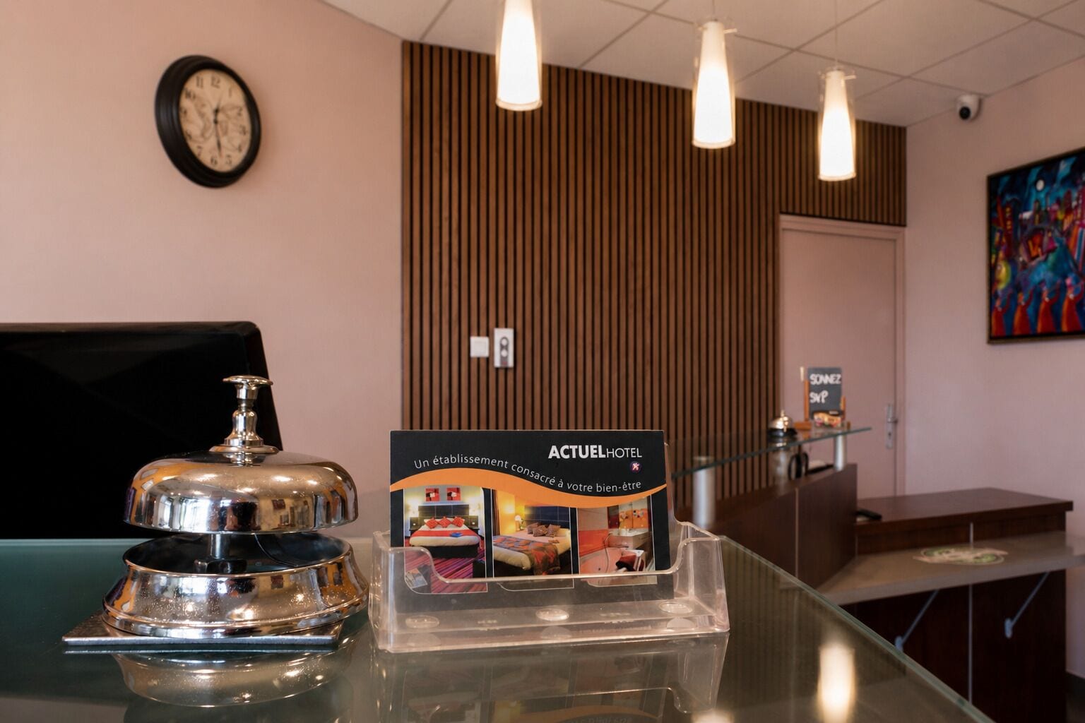 A hotel reception desk with a clock, a sign for ACTUEL HOTEL, and a clear plastic display case.