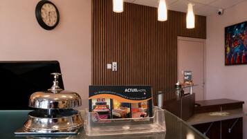 En hotellreception med en klocka, en skylt med texten ACTUEL HOTEL och ett genomskinligt plastskåp för utställning.