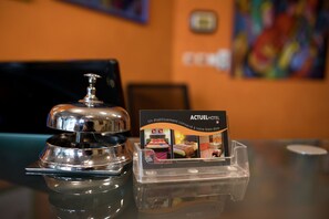 Un espace d’accueil d’hôtel avec une cloche argentée et un présentoir à brochures où sont exposées des photos de l’hôtel.