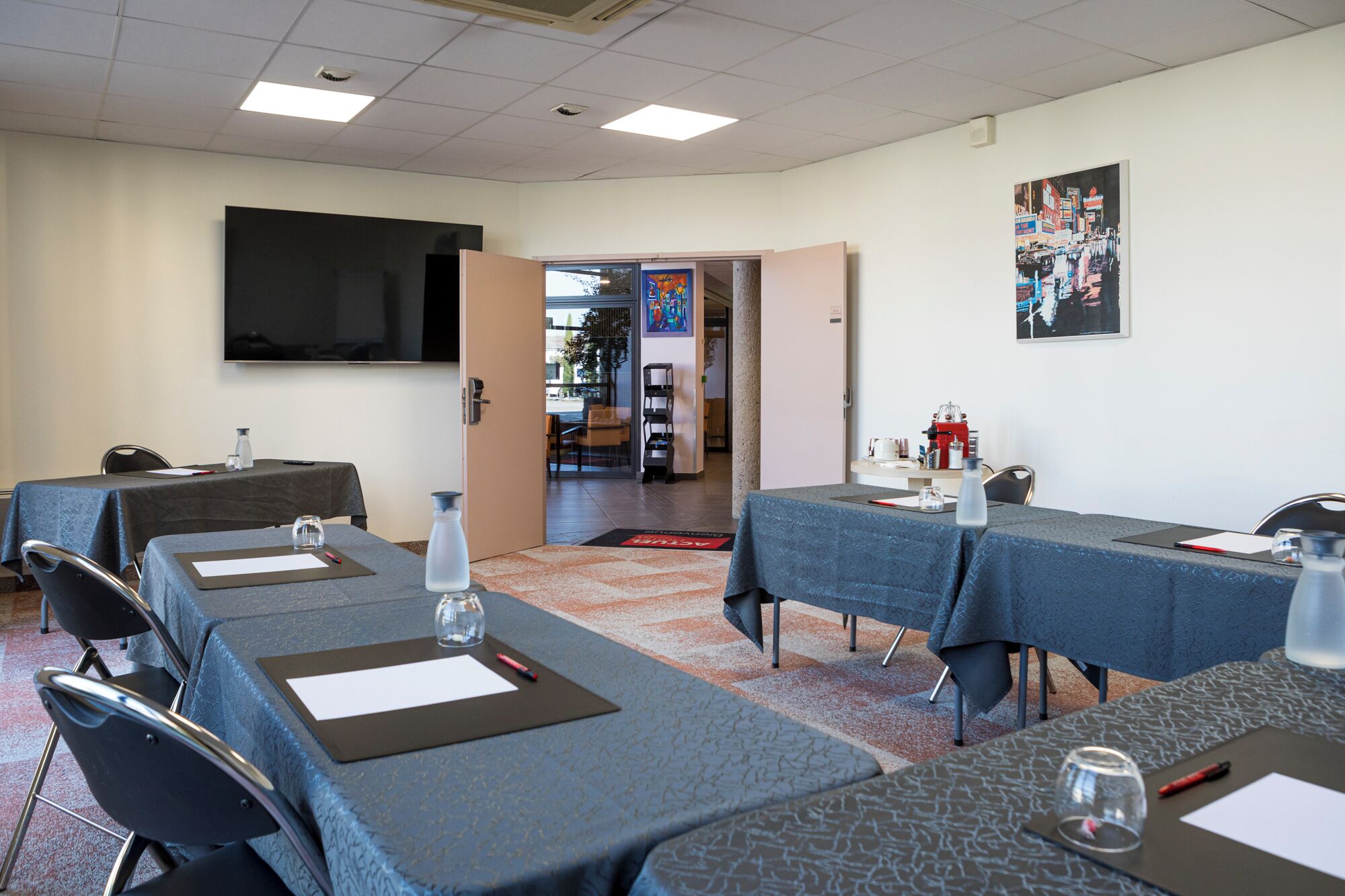 Un salón de conferencias con mesas, sillas, un televisor de pantalla plana y un cuadro en la pared.