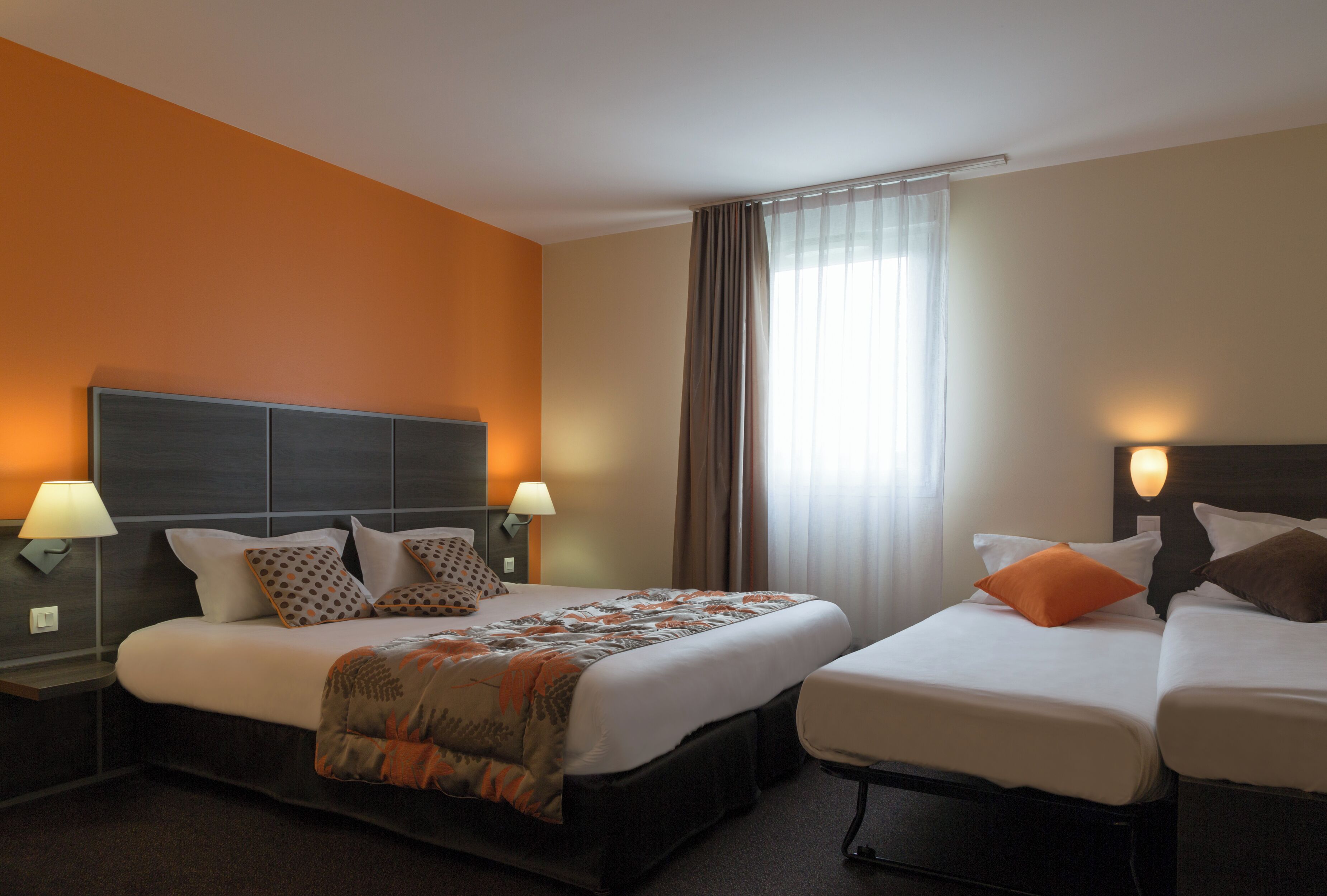 Habitació d'hotel amb dos llits, una finestra gran amb cortines i làmpades penjades a la paret.