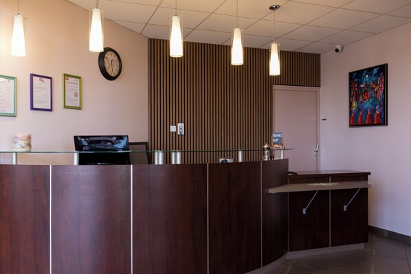 A reception desk with a clock, framed documents, and a colorful painting on the wall.