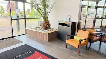 A reception area with a palm plant, a wooden bench, a glass door, and a sign indicating 'Entrance.'