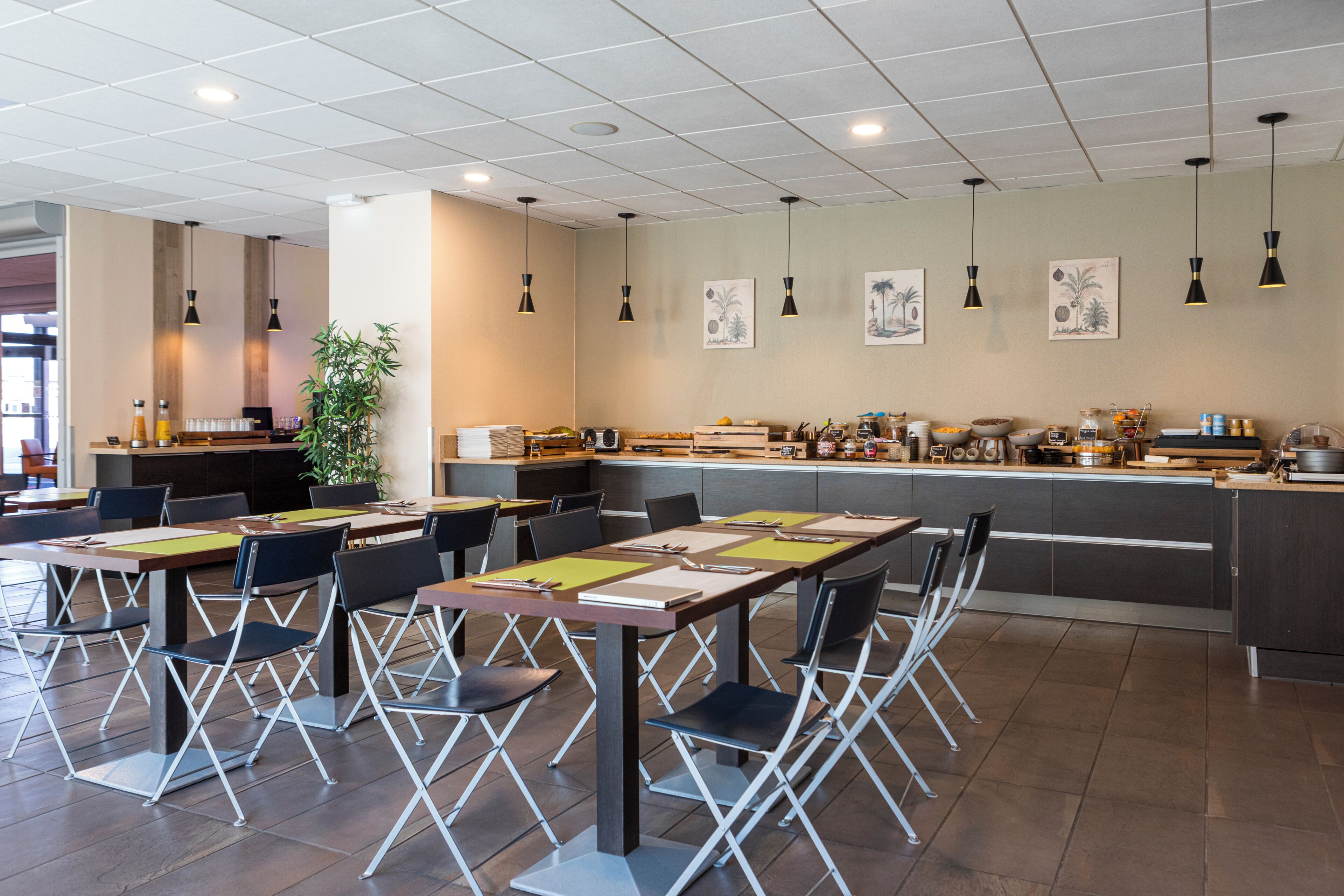 Un comedor moderno con mesas y sillas plegables, una encimera de cocina con diversos objetos y obras de arte en las paredes.