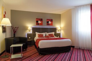 A hotel room with a large bed, two bedside lamps, a small table, and a red and black striped carpet.