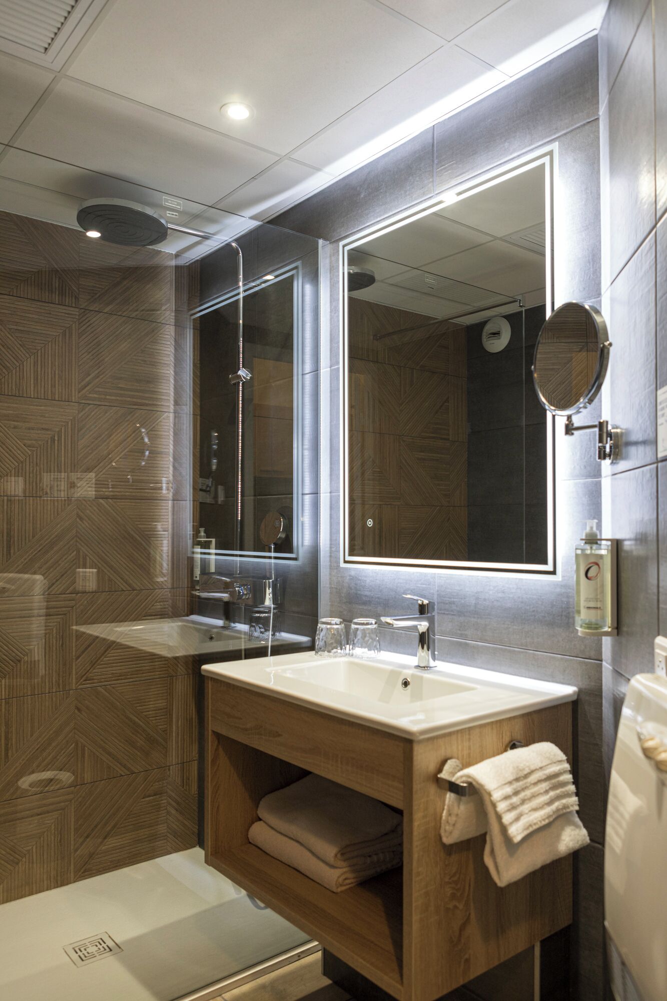 Une salle de bain moderne avec un grand miroir, deux lavabos, une douche et un meuble-lavabo en bois.
