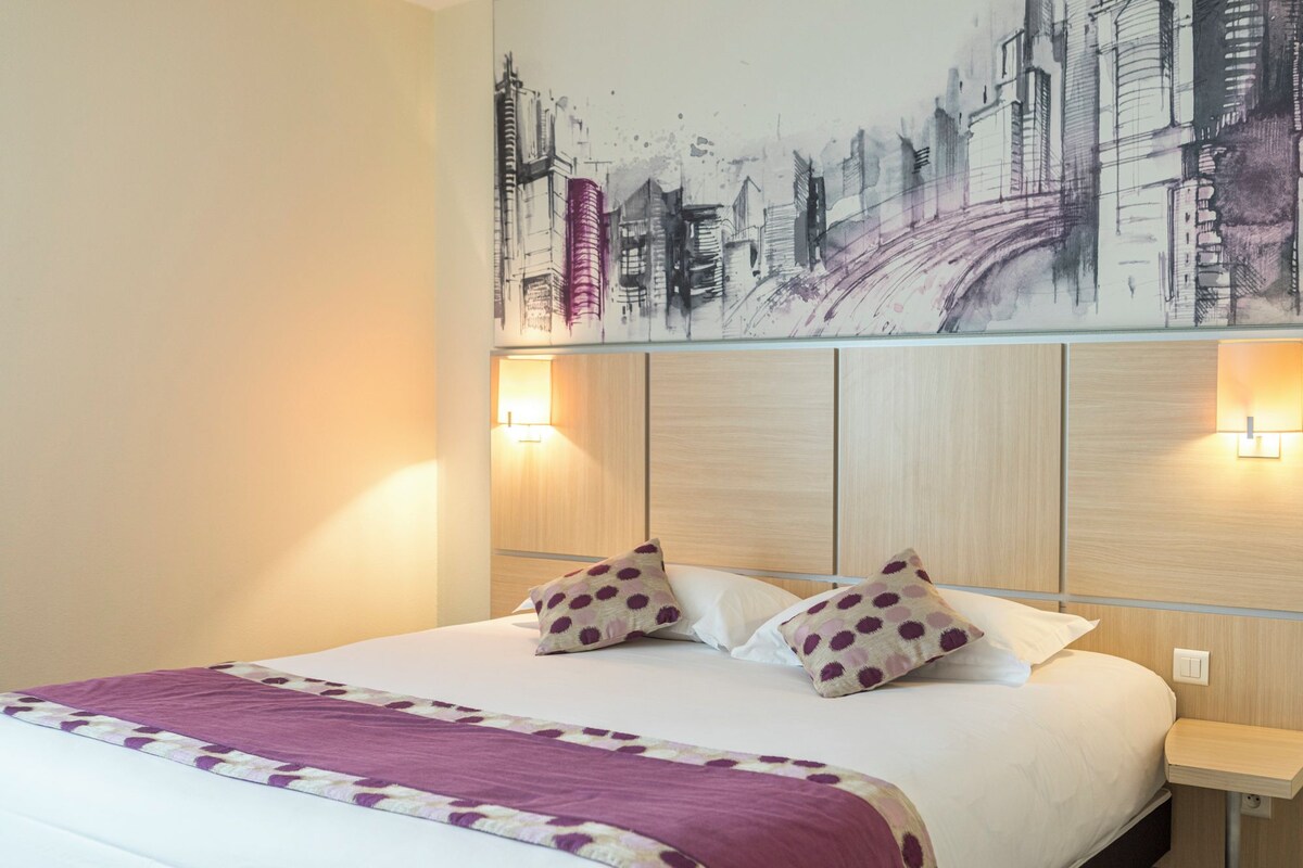 A hotel room with a bed, two pillows, a headboard, and a wall-mounted artwork.