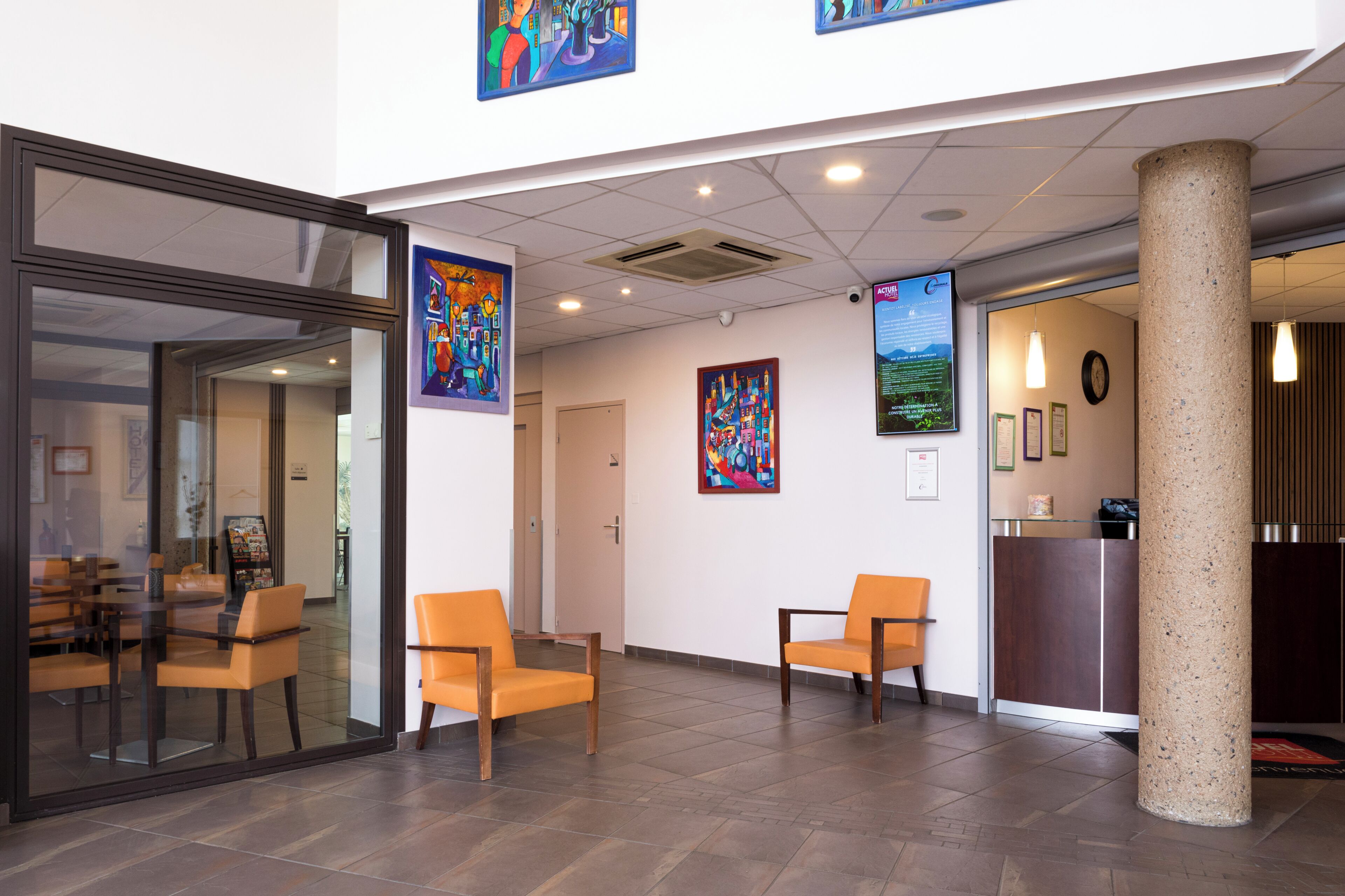 A reception area with a glass partition, wooden chairs, a reception desk, and artwork on the walls.
