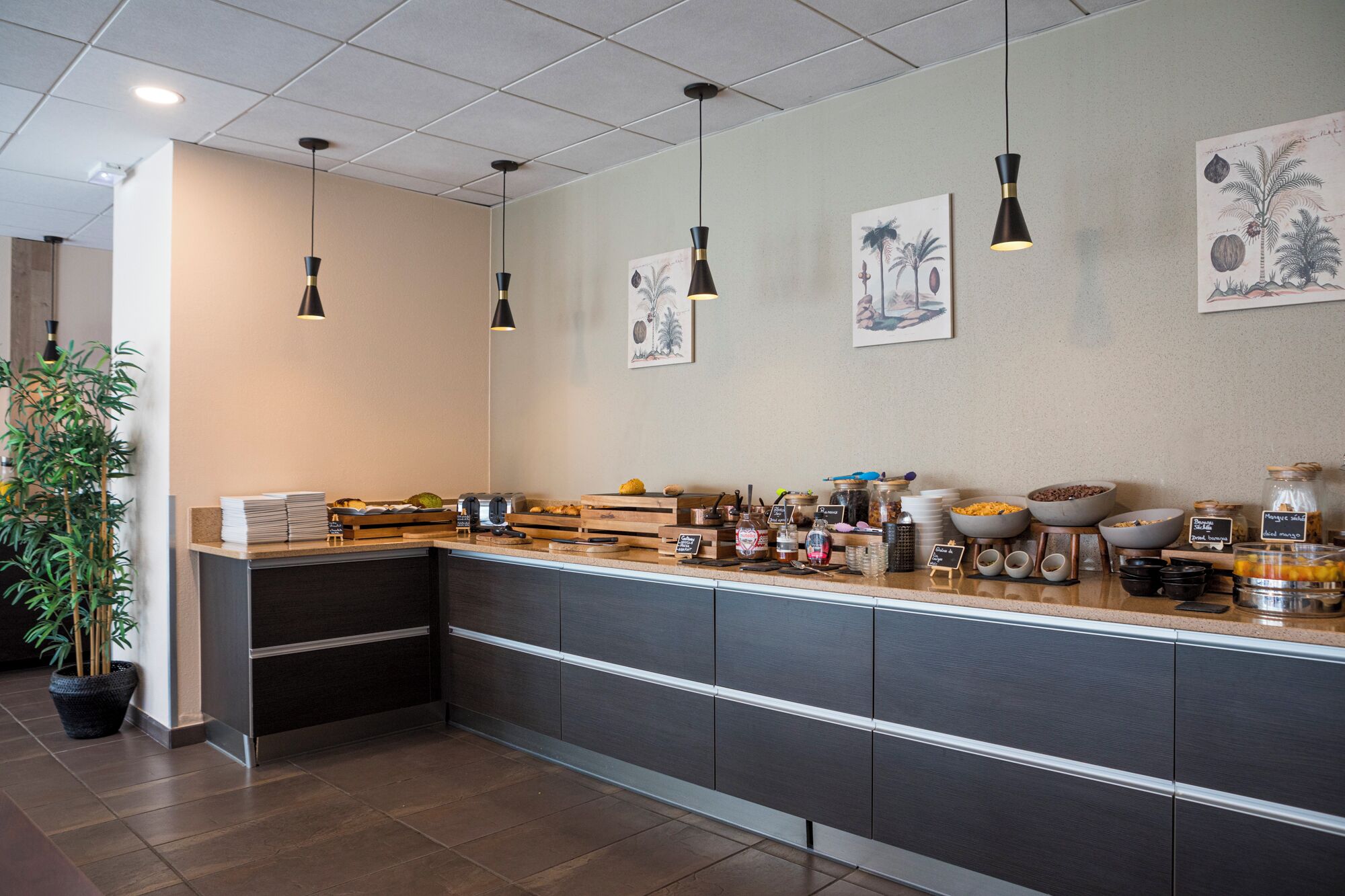 A modern kitchen with a long counter, various food items, and hanging pendant lights.