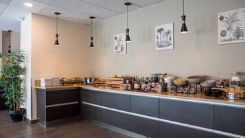 A modern kitchen with a long counter, various food items, and hanging pendant lights.