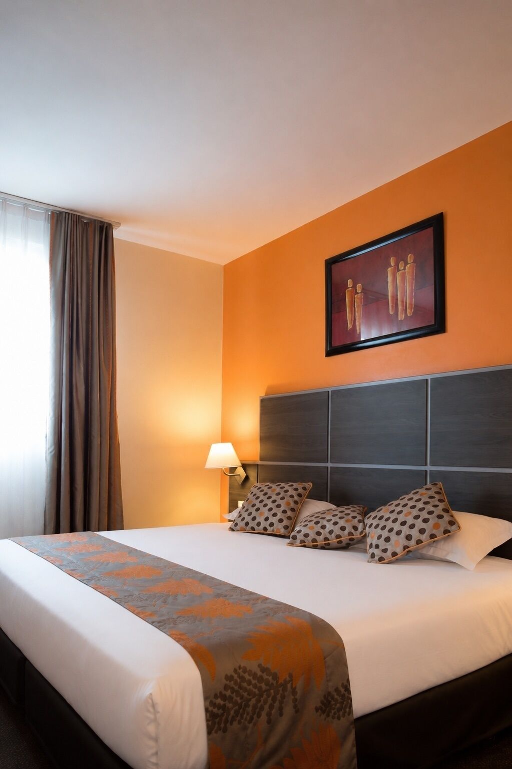 Une chambre d’hôtel avec un grand lit, une tête de lit, une œuvre d’art accrochée au mur et une fenêtre avec des rideaux.