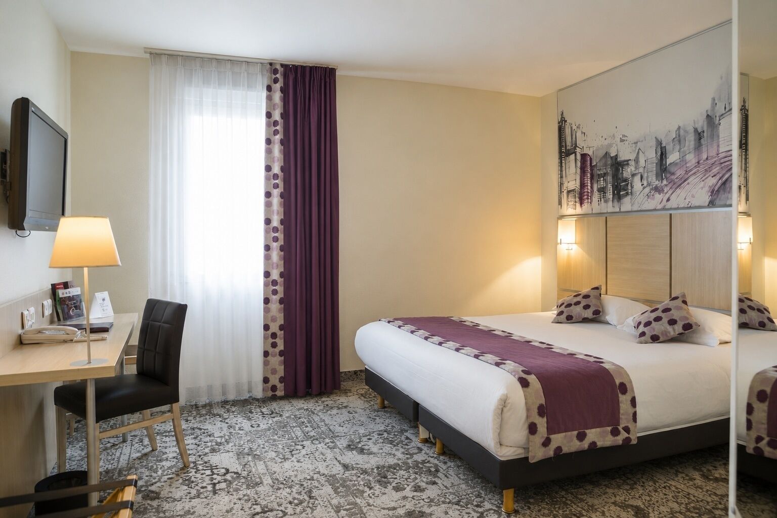 Habitación de hotel con cama, escritorio, silla y televisor.