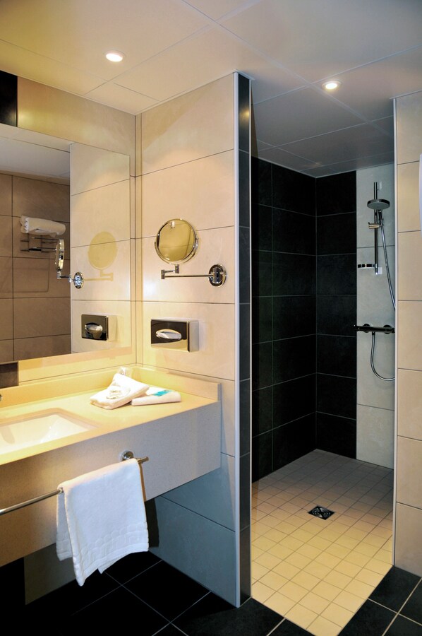 A modern bathroom with a large mirror, a sink, a towel rack, and a shower area.