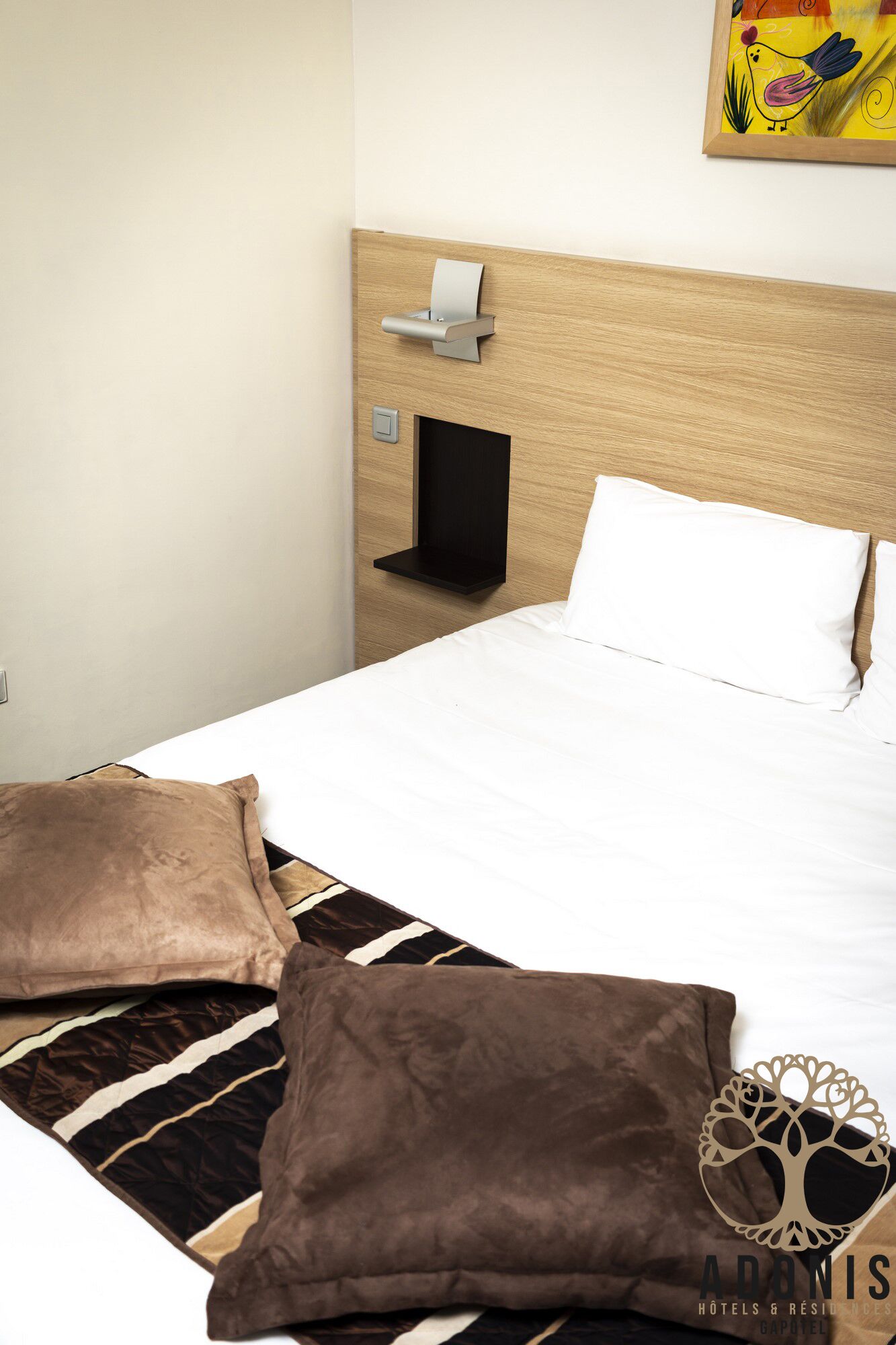 A neatly made bed with two pillows, a bedside table with a lamp, and a wall-mounted shelf.