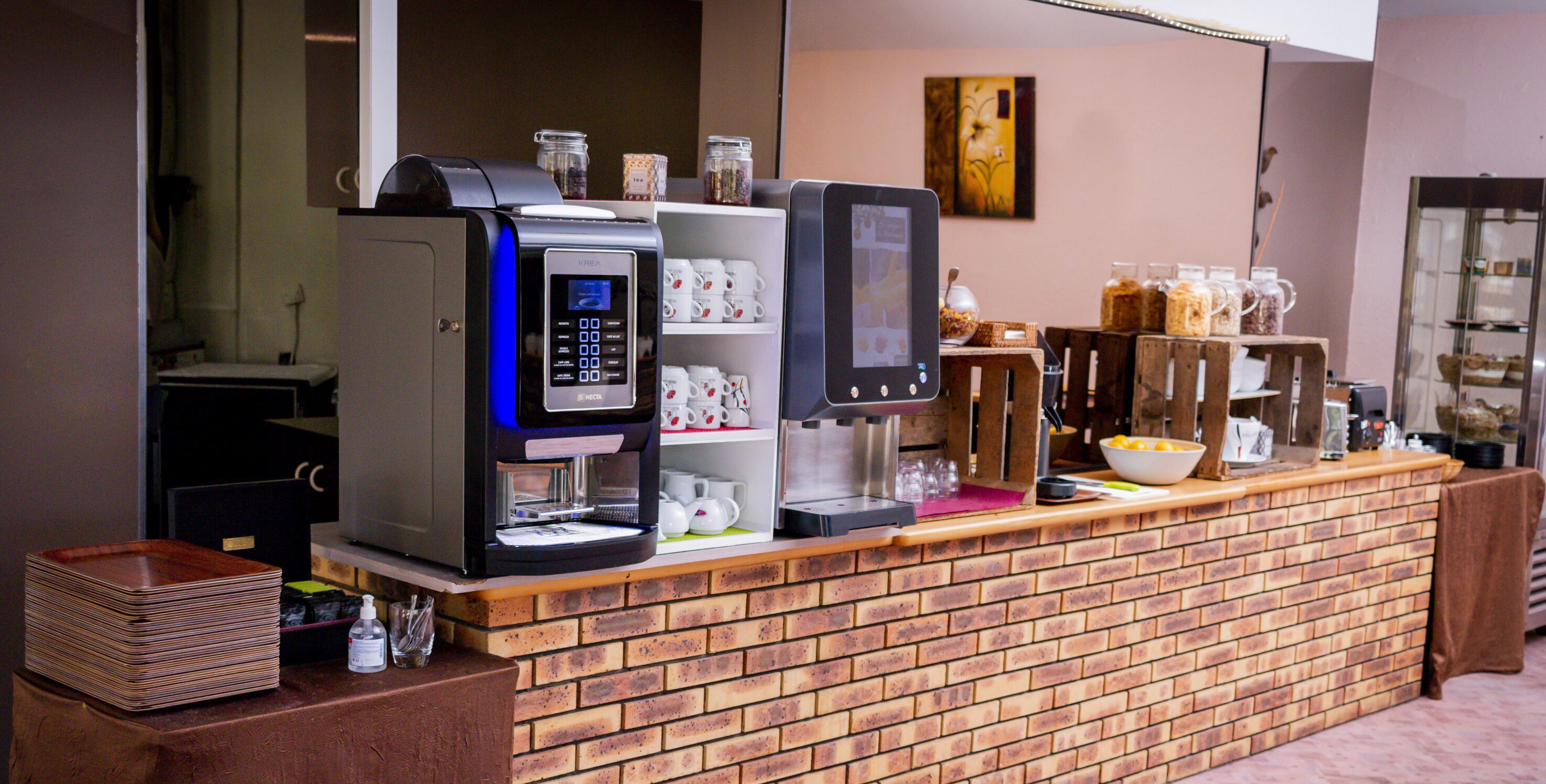 A coffee station with two espresso machines, a coffee dispenser, and a variety of mugs and containers.
