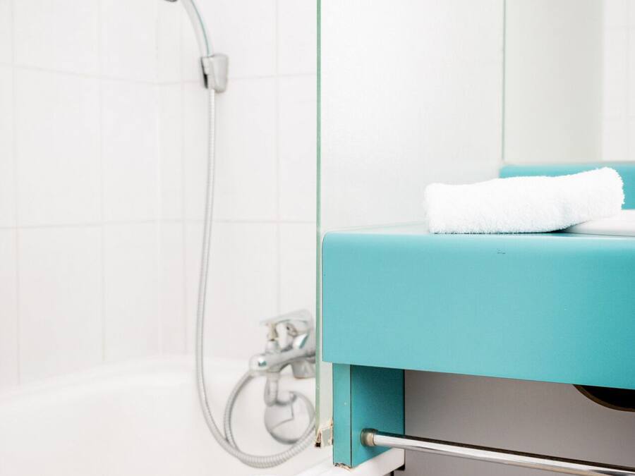 A bathroom with a white bathtub, a shower head, and a towel on the edge.