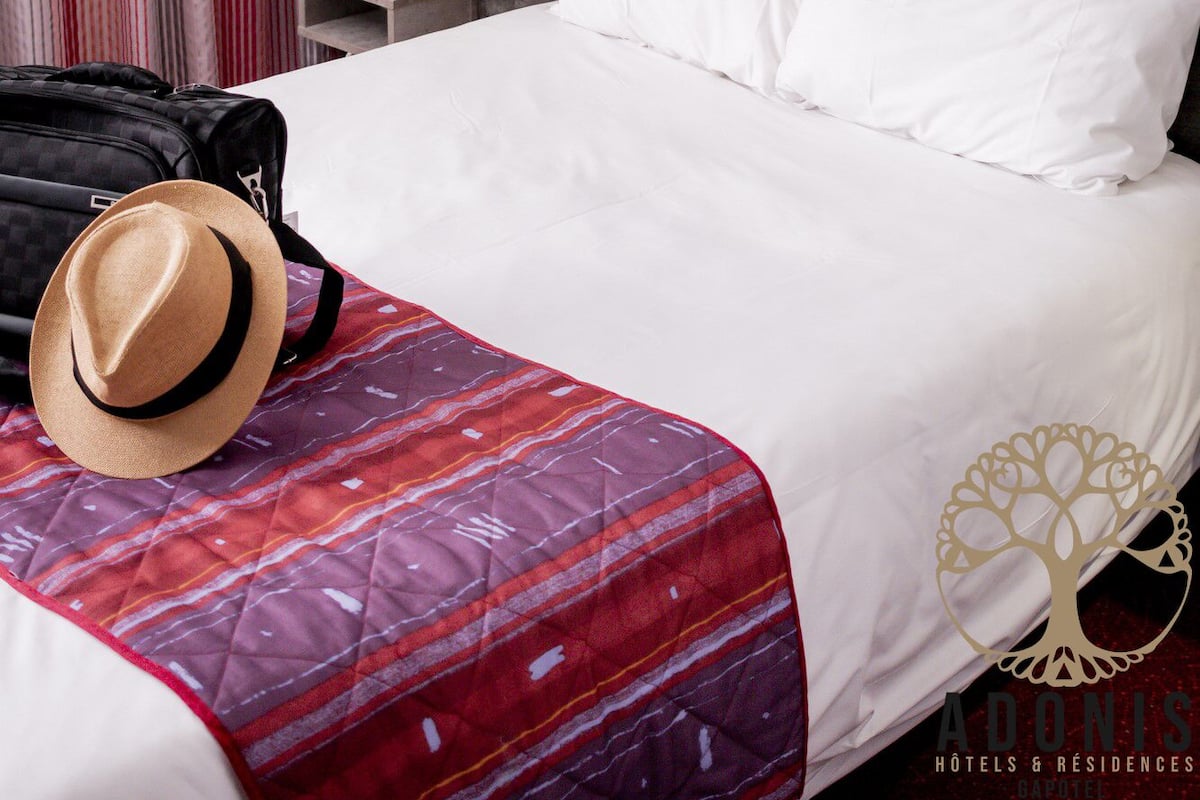 Una habitación de hotel con una cama, un sombrero, una maleta y un cuadro en la pared.