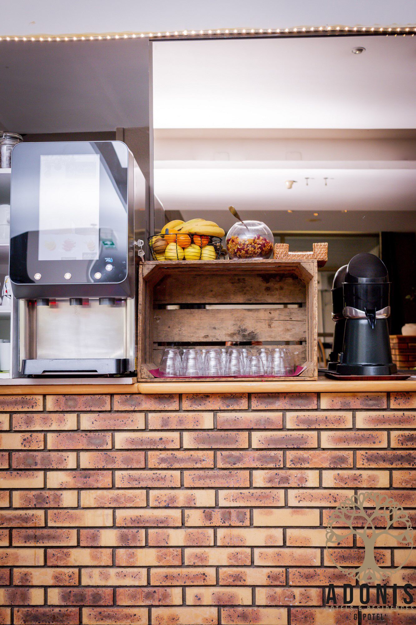 Pared de ladrillo con una máquina de café, una vitrina con frutas y una cafetera.