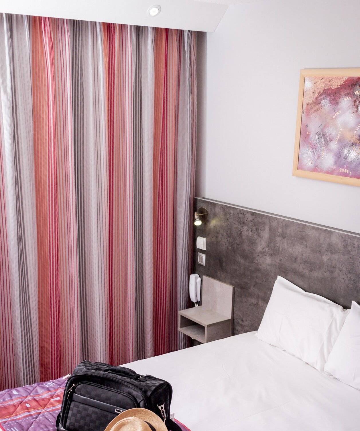 Habitación de hotel con cama, cabecera, mesita de noche con lámpara, teléfono y maleta sobre la cama.