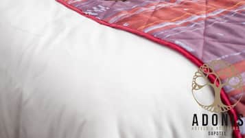 A bed with a striped curtain in the background, a black bag, and a straw hat on a patterned bedspread.