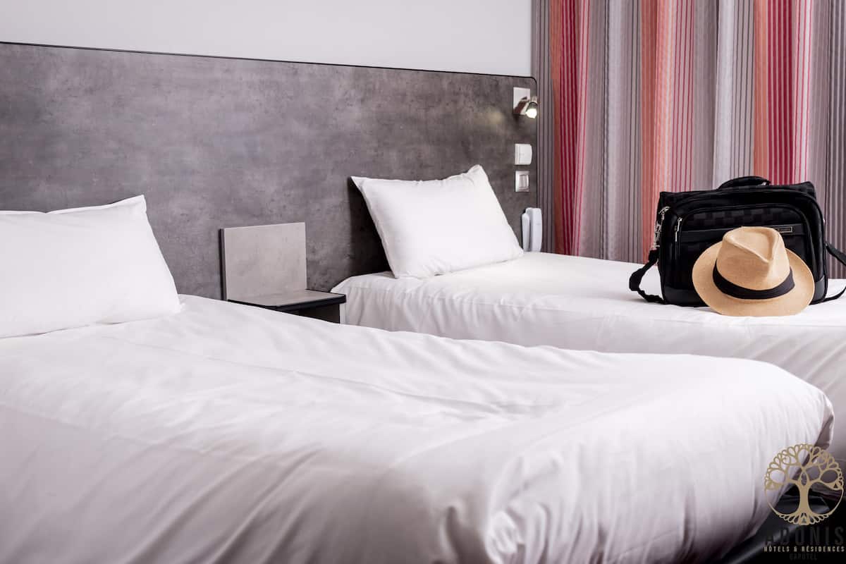 Habitación de hotel con dos camas, cabecero, mesita de noche y cortina a rayas.