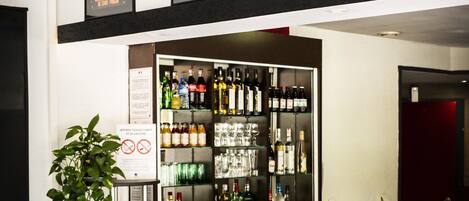 Zona de bar con varias botellas de licores y vasos, un cartel que prohíbe fumar y tres carteles enmarcados sobre la barra.
