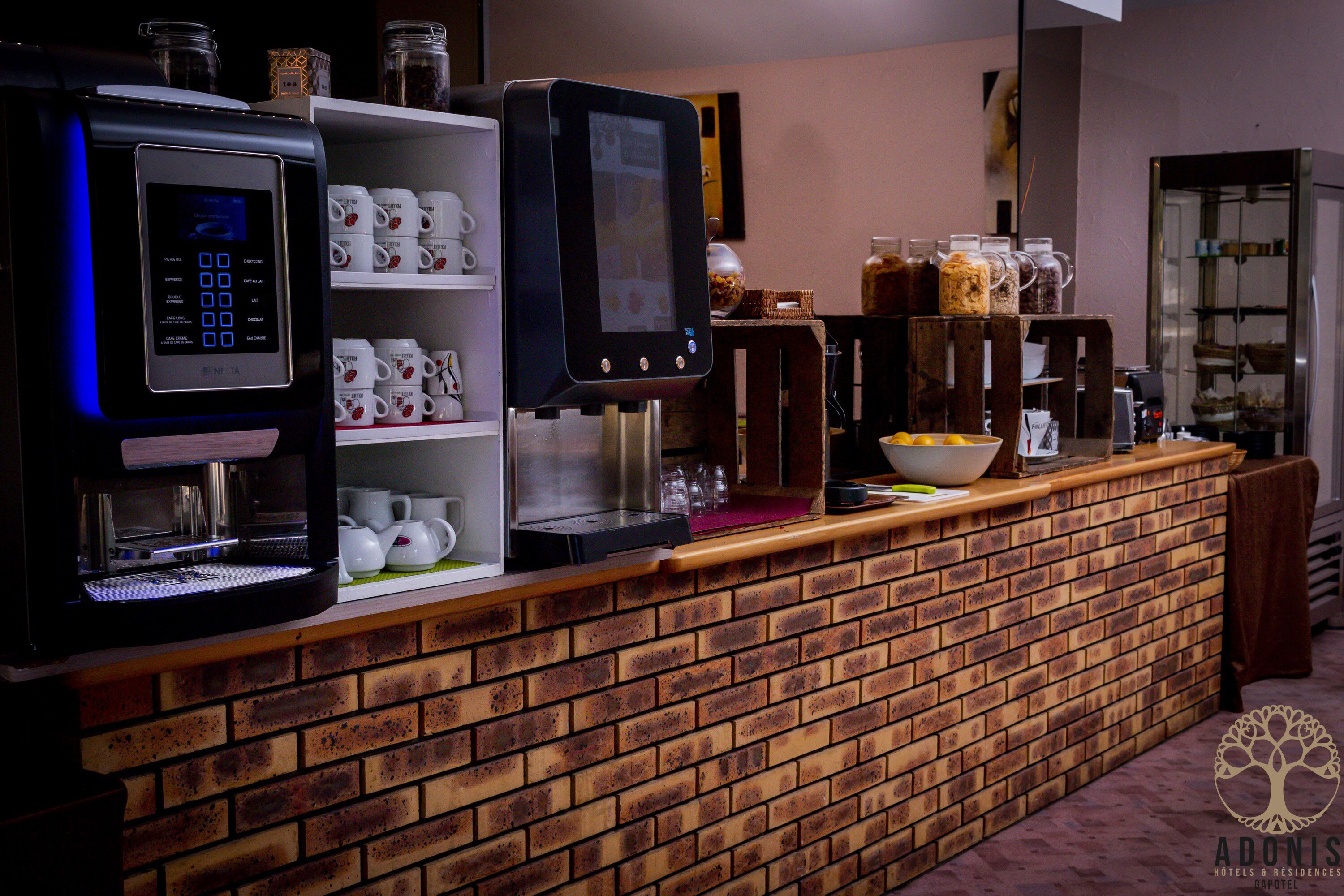 En kaffestation med två espressomaskiner, en digital kaffebryggare och en display. Det finns hyllor med kaffemuggar och en skål med citroner.
