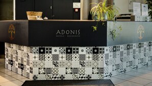 A reception desk with a black and white patterned design, a plant, and a sign indicating the hotel name 'ADONIS'. - Adonis Gapotel (Gap)