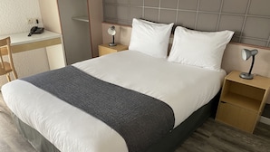 Een netjes opgemaakt bed met wit en grijs beddengoed, twee nachtkastjes met lampen, een bureau met telefoon en een stoel.