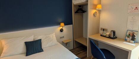 Habitación de hotel con cama, lámparas de noche, escritorio, silla, armario y un cartel en la pared.