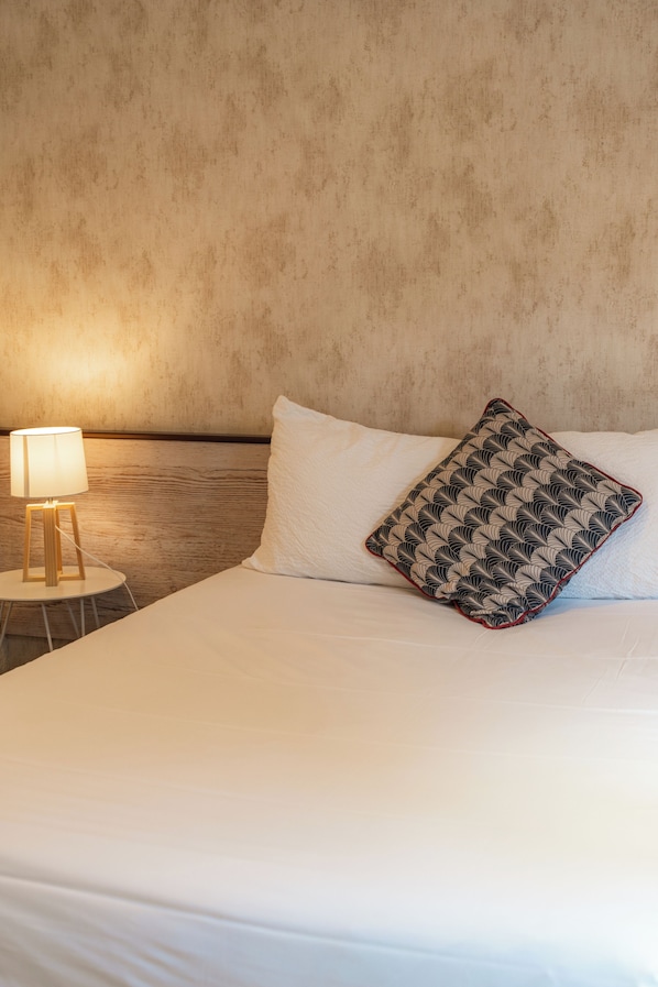 A neatly made bed with white bedding and a patterned pillow, a bedside lamp, and a textured wall.