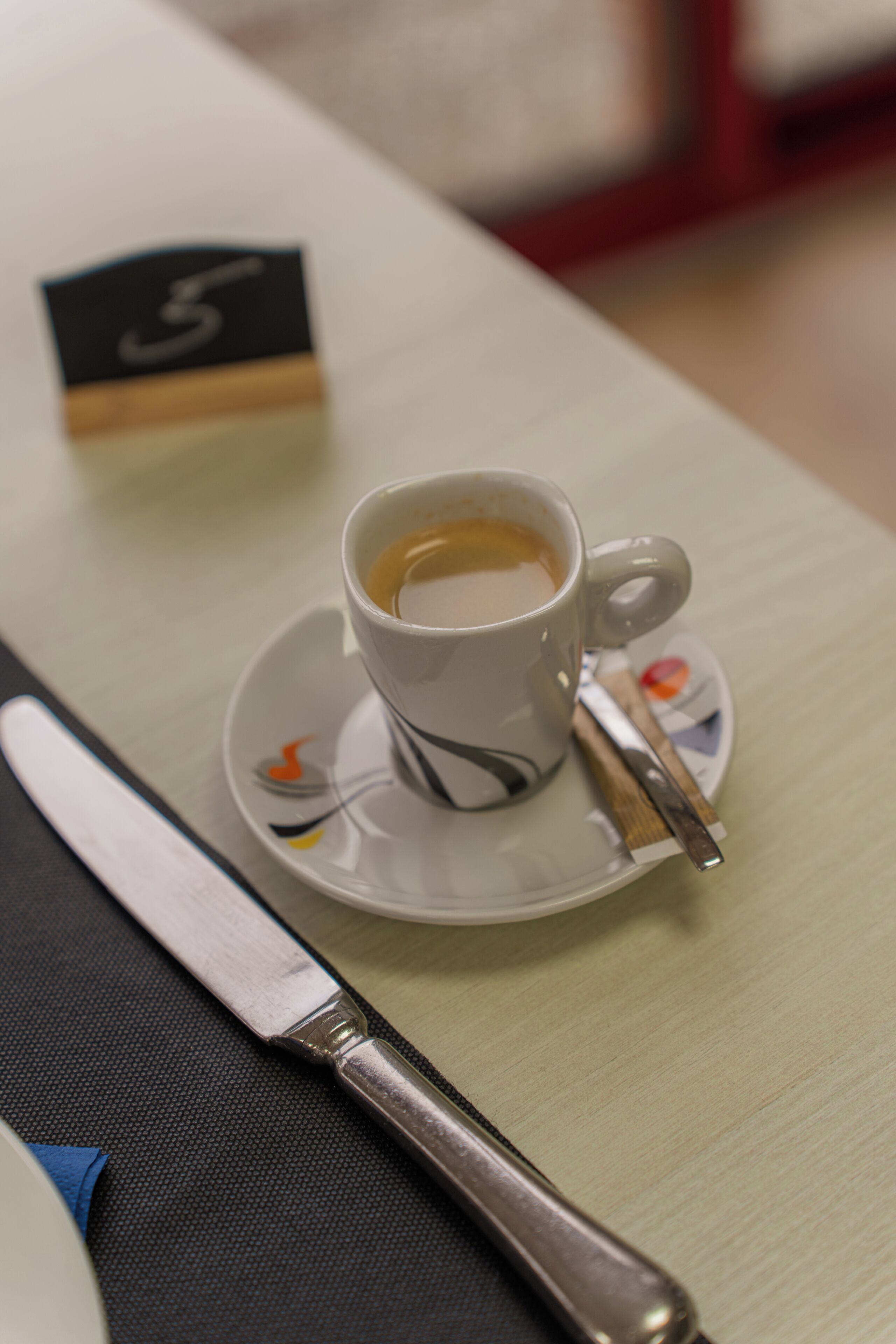 Eine Tasse Kaffee auf einem Untertasse mit einem Löffel, einem Messer und einer Nummer auf einem Tisch.