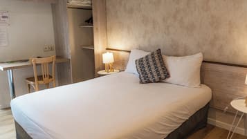 A neatly made bed with white bedding, a wooden chair, a bedside table with a lamp, and a shelf with items.