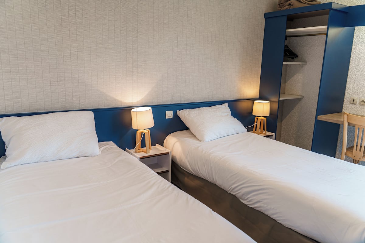 Two single beds with white linens, wooden nightstands with lamps, and a blue headboard.