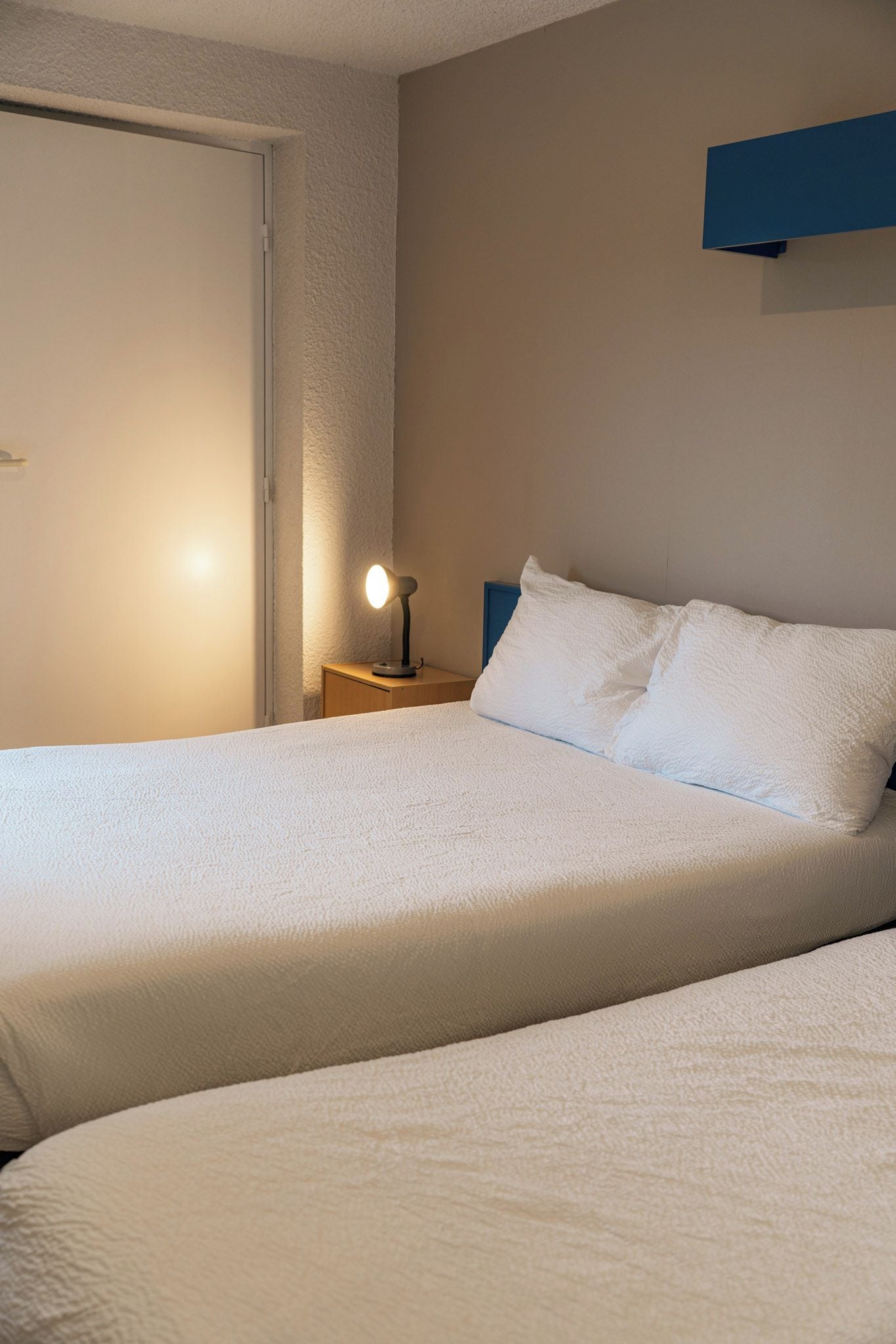 Una cama doble con edredón blanco, una lámpara de noche y una mesita de madera.