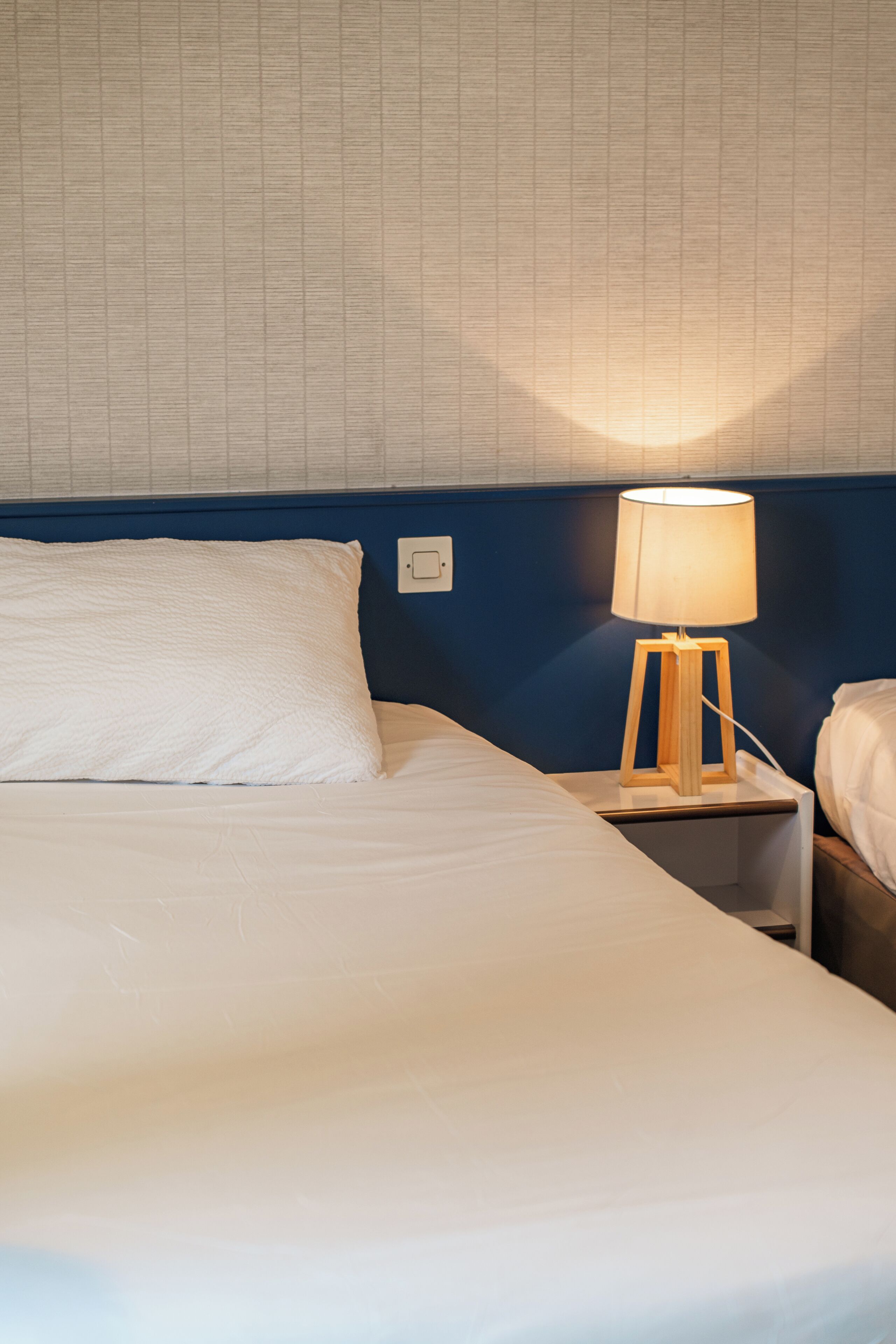 A hotel room with a bed, a nightstand with a lamp, and a wall with a grid pattern.