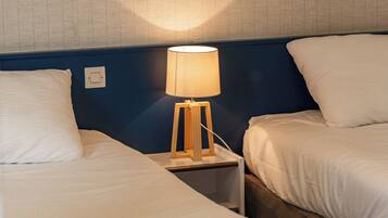 A hotel room with two beds, a bedside table with a lamp, and a wall with a textured pattern.