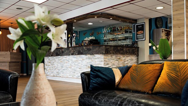 Een bar met een toonbank, barstoelen en een zithoek met een bank en een bloevas.