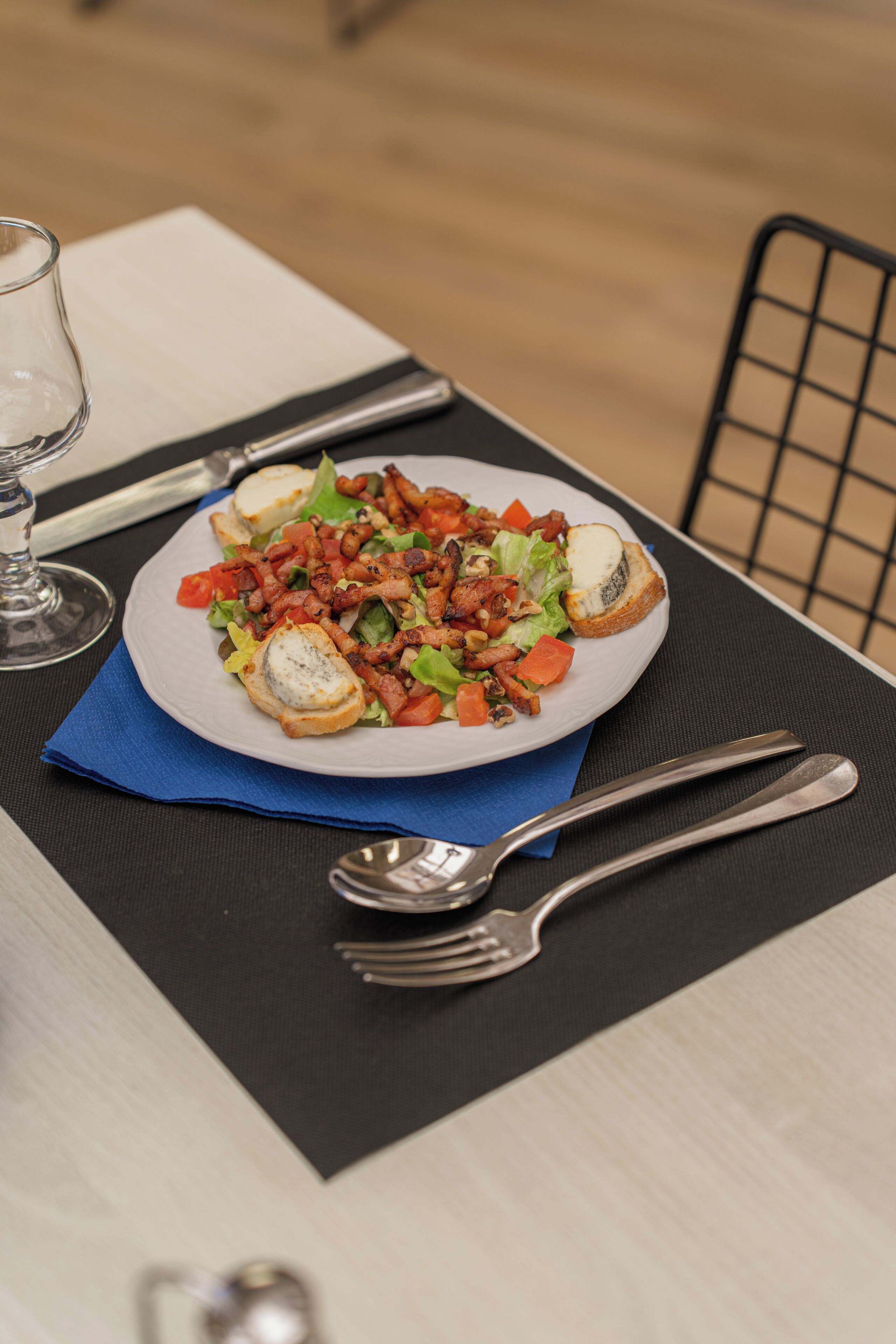 Un plato de comida sobre una mesa, con servilleta, cubiertos y una copa.