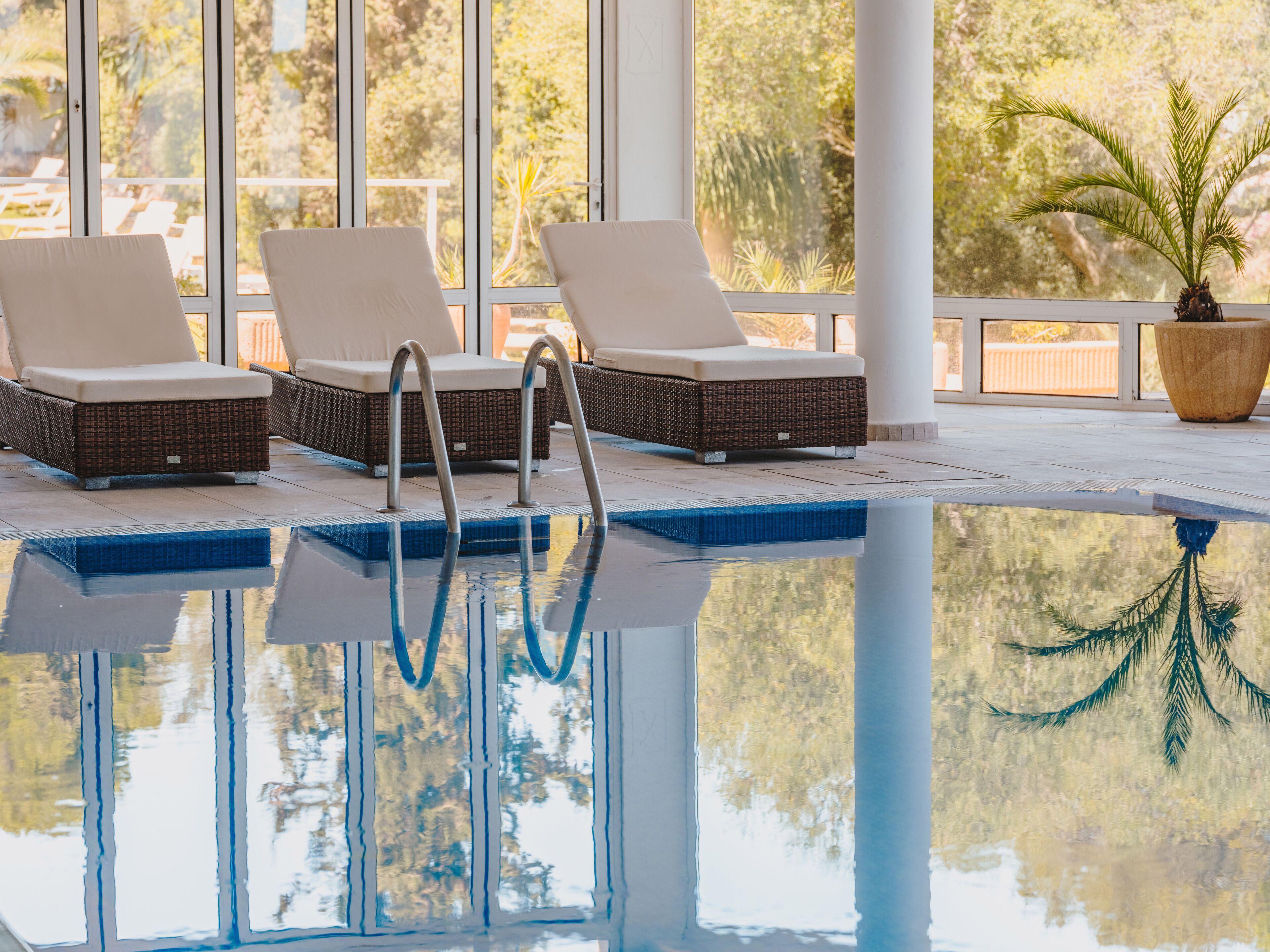 A pool area with lounge chairs and a reflection of trees.