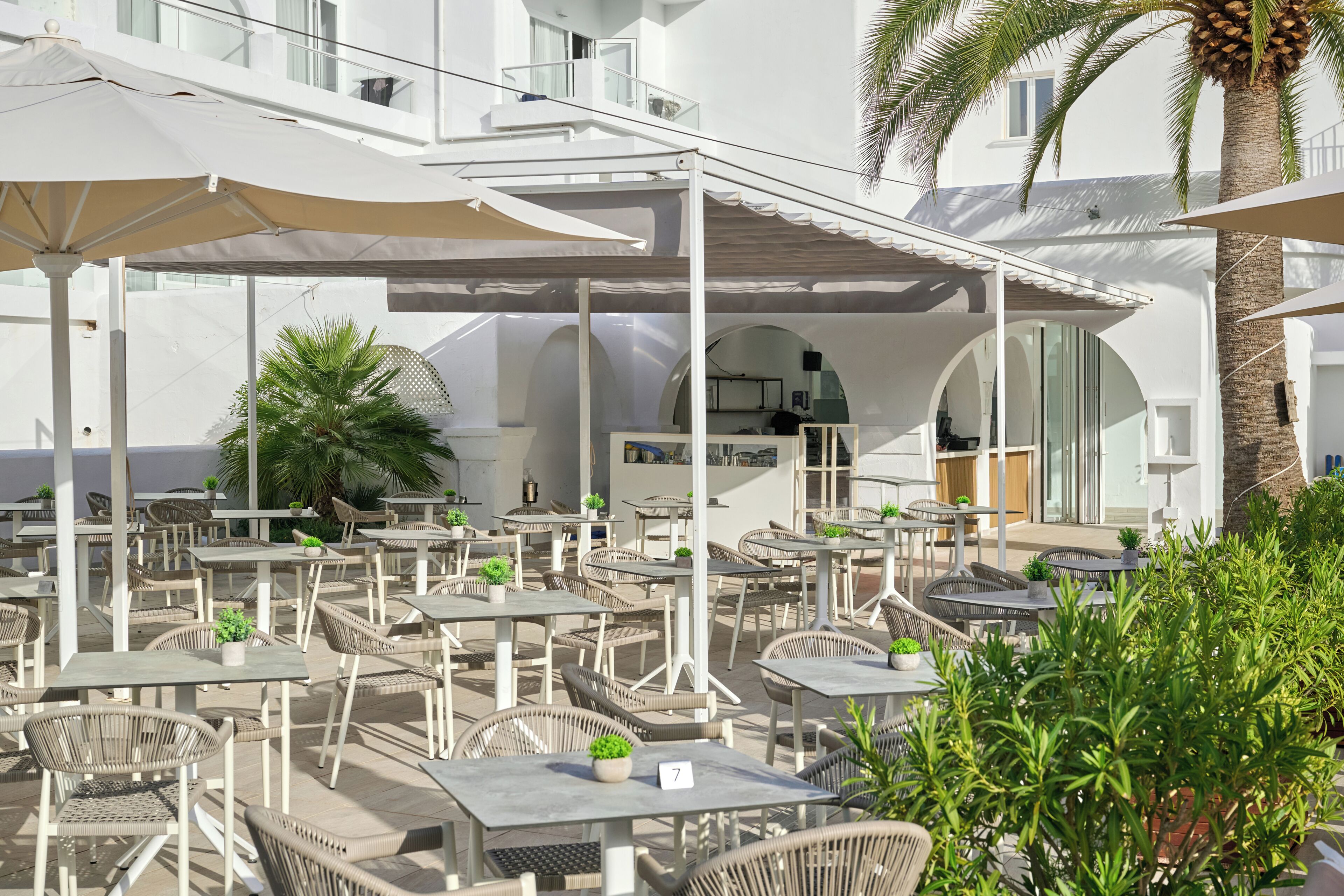 Een terras met tafels en stoelen, parasols en potplanten.
