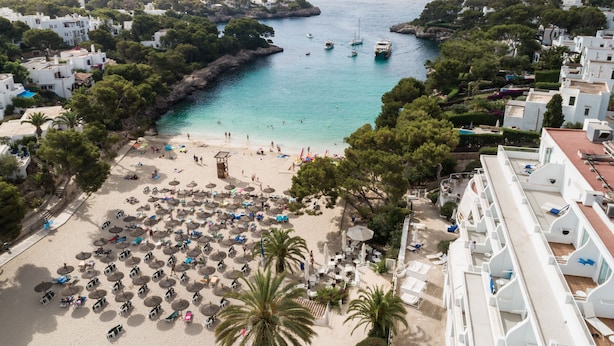 A beach with numerous umbrellas and sun loungers, a clear view of the sea, and buildings in the background. - Grupotel Rocador (Santanyi)