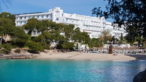 A large white hotel with multiple balconies and a beach area with sun loungers. - Grupotel Rocador (Santanyi)
