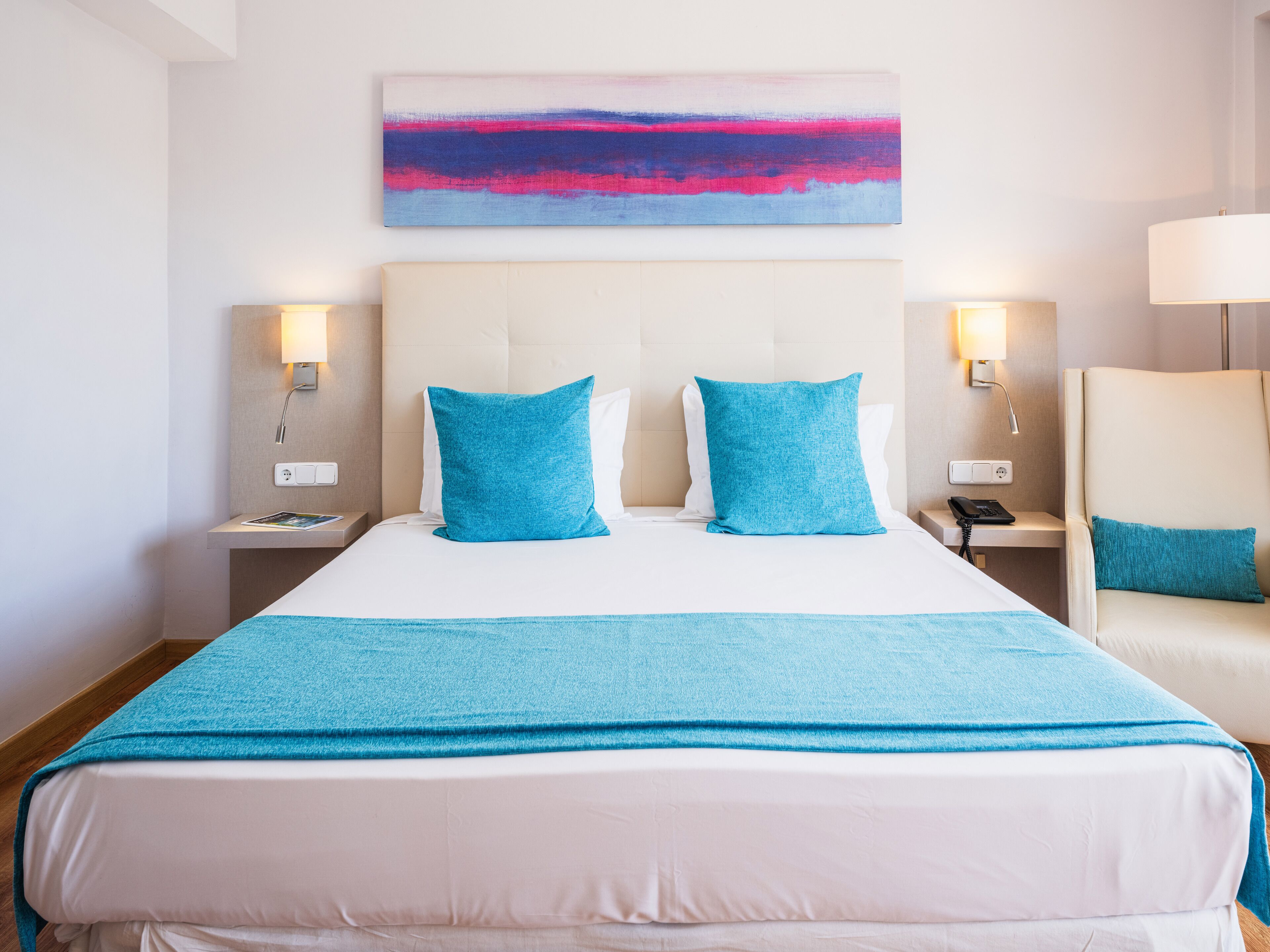 Une chambre d’hôtel avec un grand lit, deux tables de chevet, une chaise et un tableau au mur.