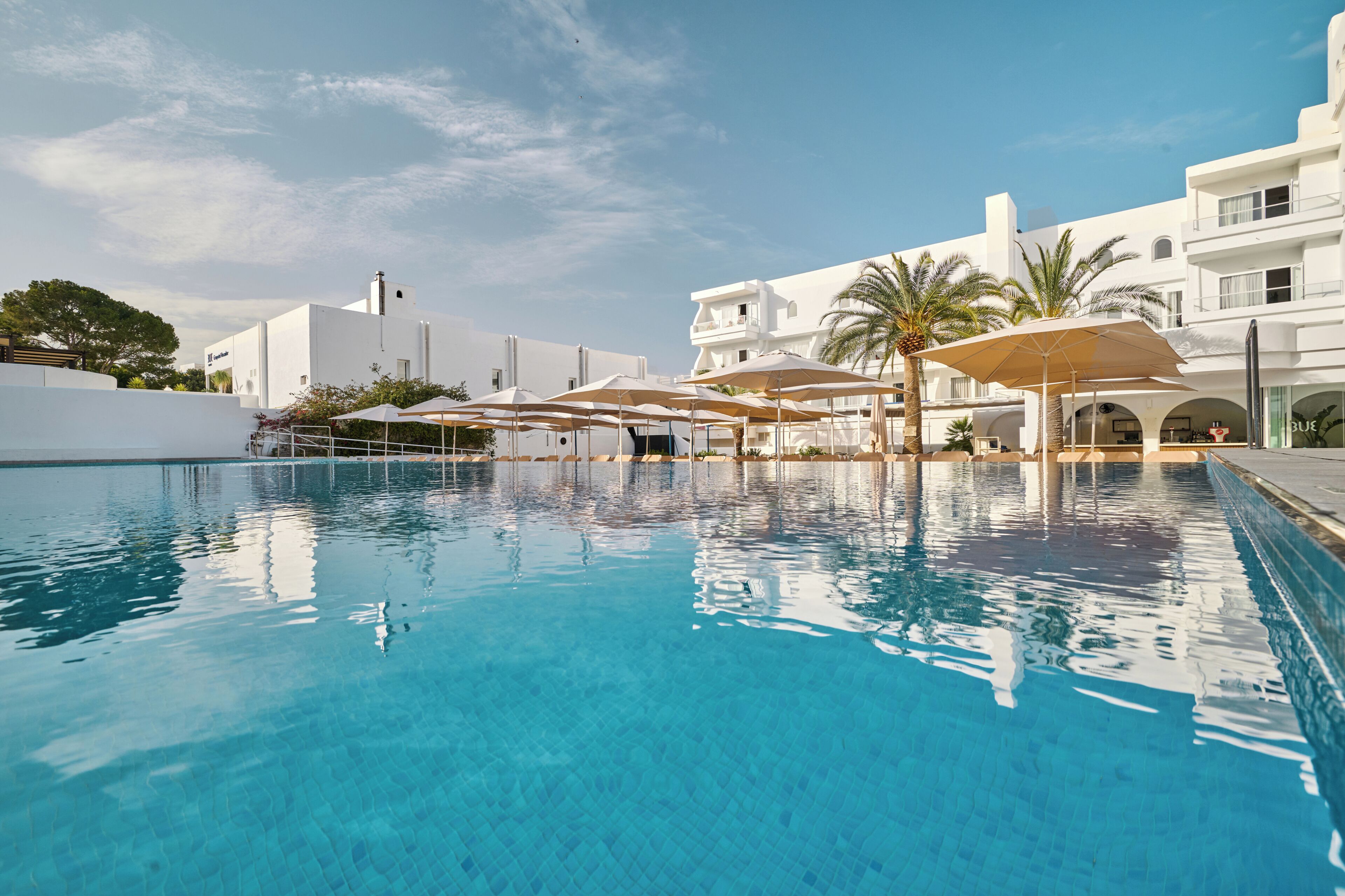 Una piscina con agua azul cristalina, rodeada de edificios blancos y palmeras.