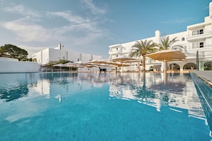 Une piscine à l’eau d’un bleu cristallin, entourée de bâtiments blancs et de palmiers.