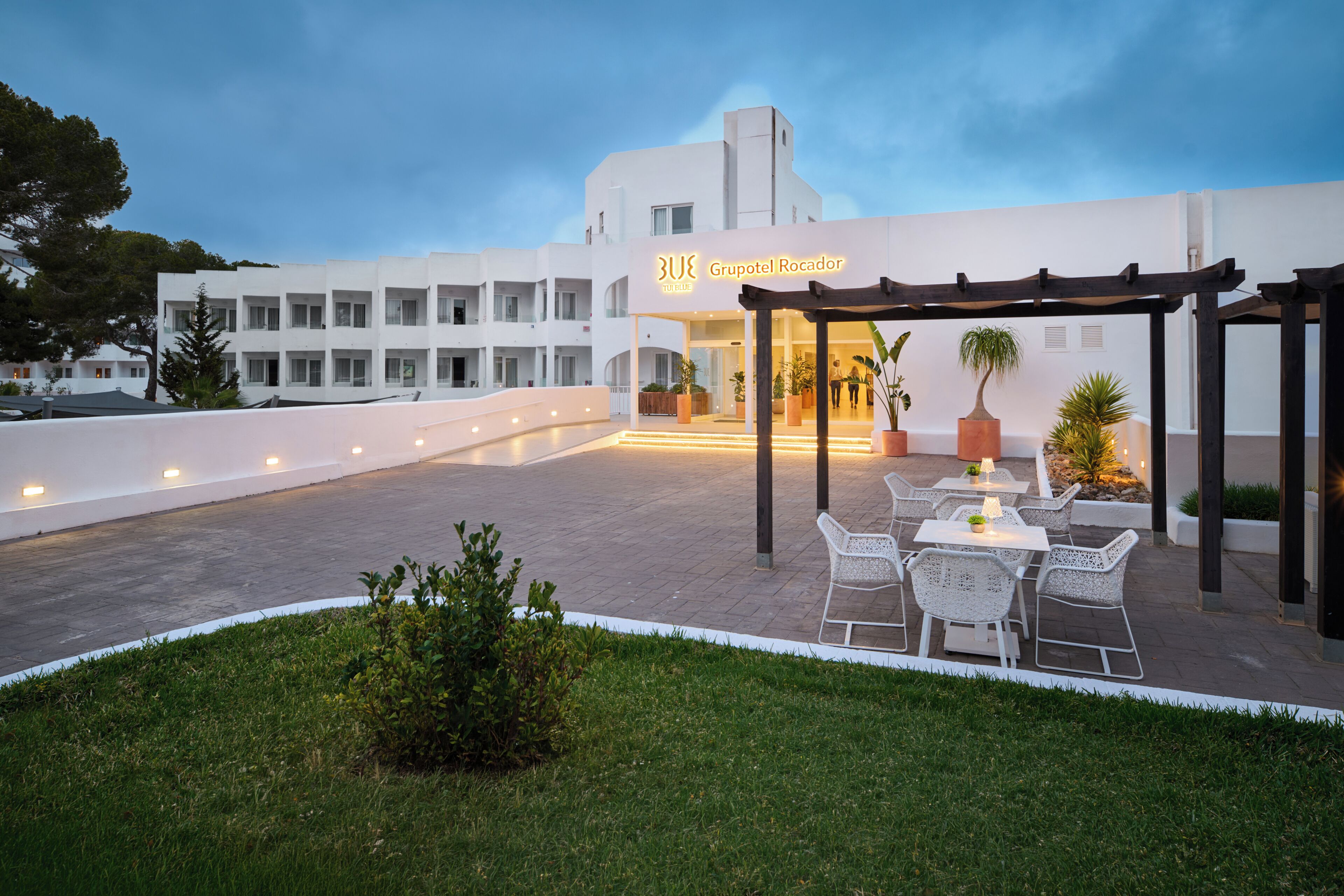 Esterno di un hotel con una zona salotto coperta, un ingresso e un prato curato.