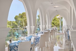 Un restaurant avec des arches blanches, des nappes bleues et une vue sur les arbres.